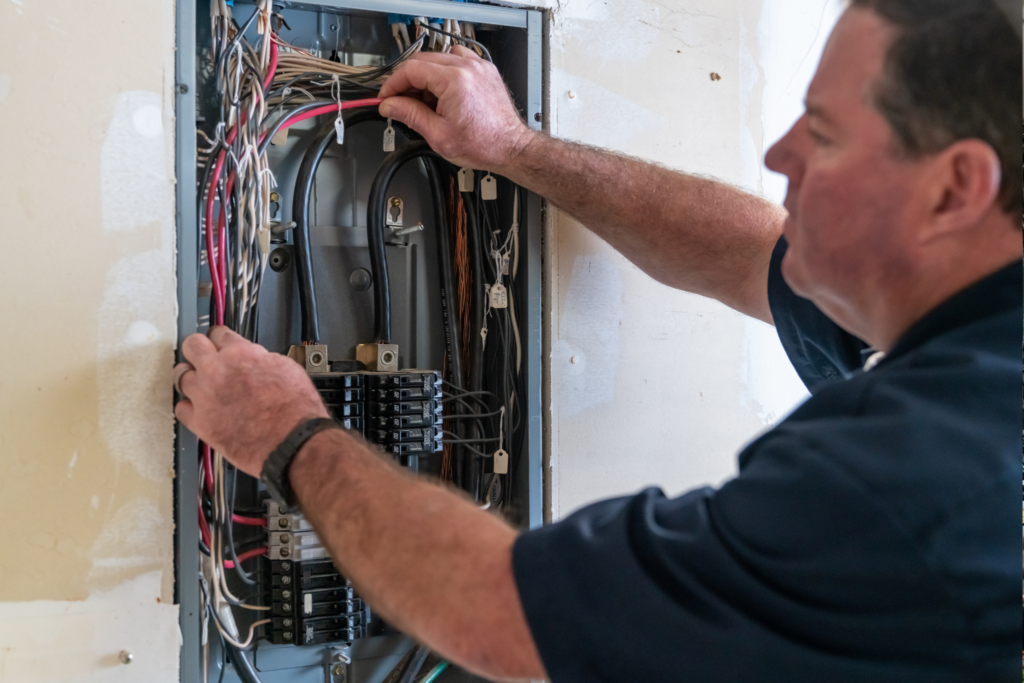 %Imagetitle% | Advanced Home Services An electrician inspects and adjusts wiring inside an open electrical panel mounted on a wall.